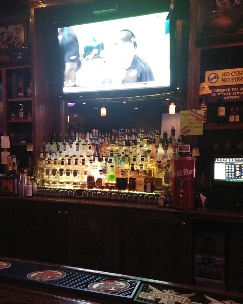 The back bar at night, bottles lit from below under a big TV