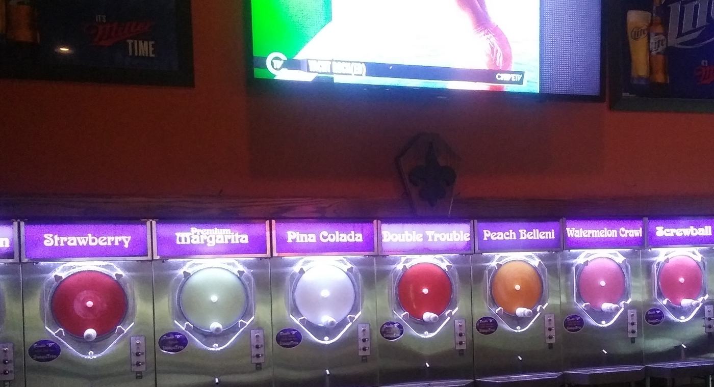 The daiquiri machines in a row, each flavor lit from inside under a purple label