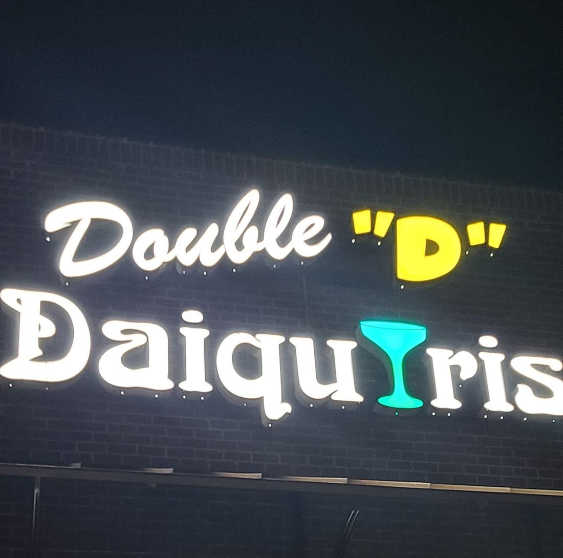 The lit Double D Daiquiris sign on the brick front of the bar at night
