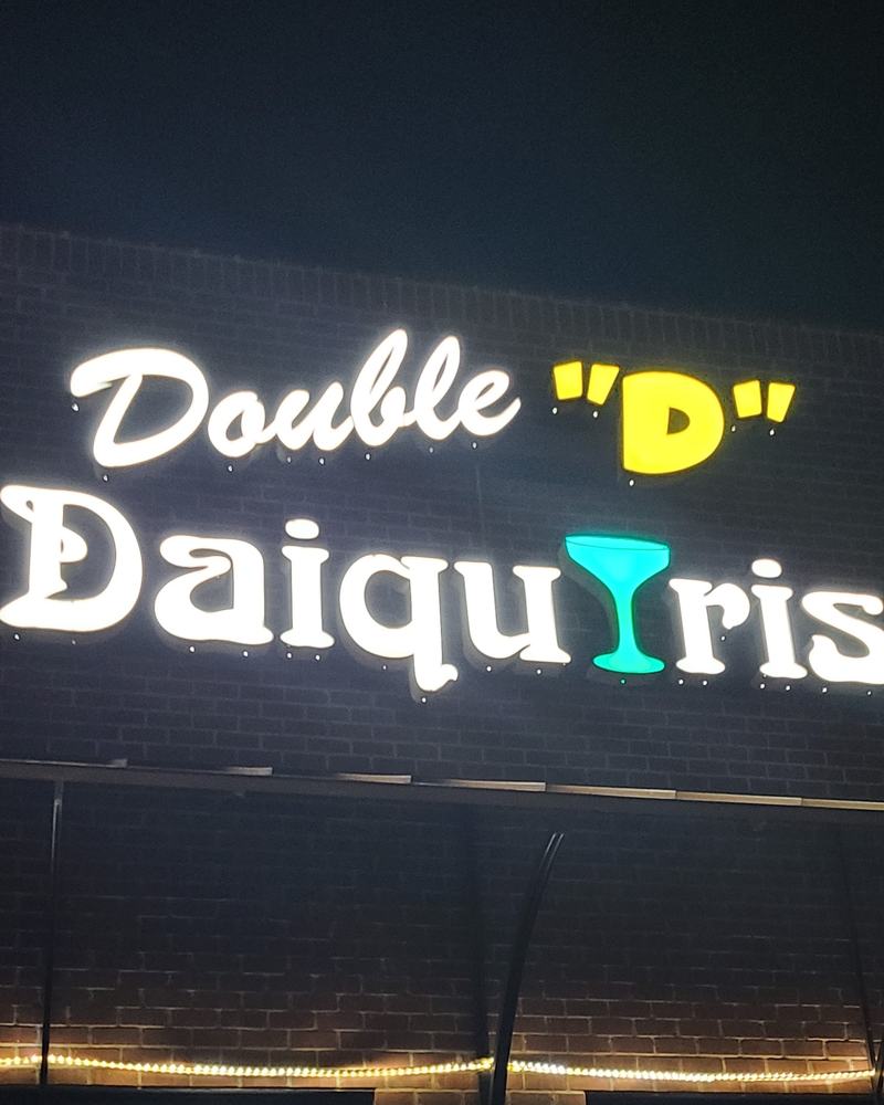 The Double D Daiquiris sign glowing on the brick front at night